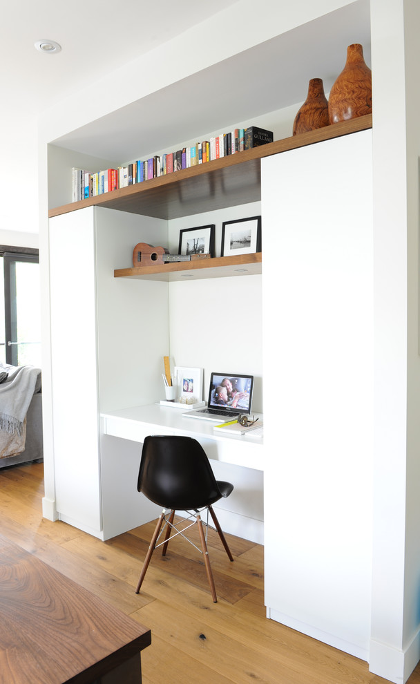 Imagen de despacho actual con paredes blancas, suelo de madera en tonos medios y escritorio empotrado
