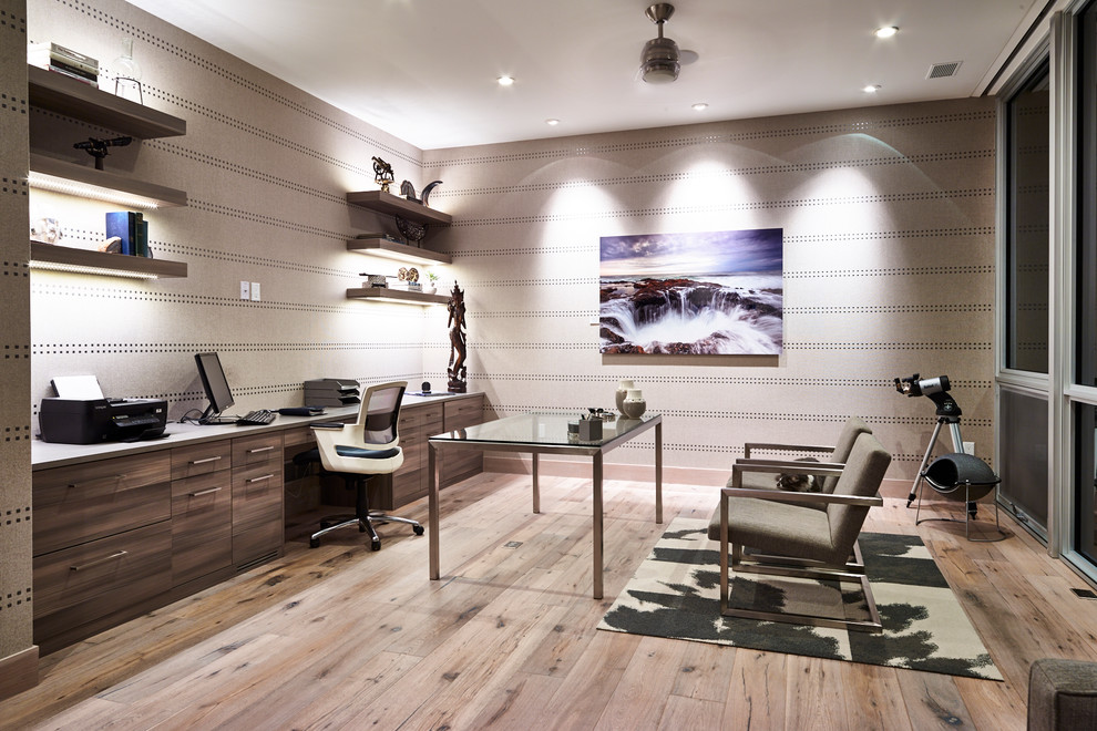Diseño de despacho actual grande sin chimenea con paredes grises, suelo de madera clara y escritorio empotrado