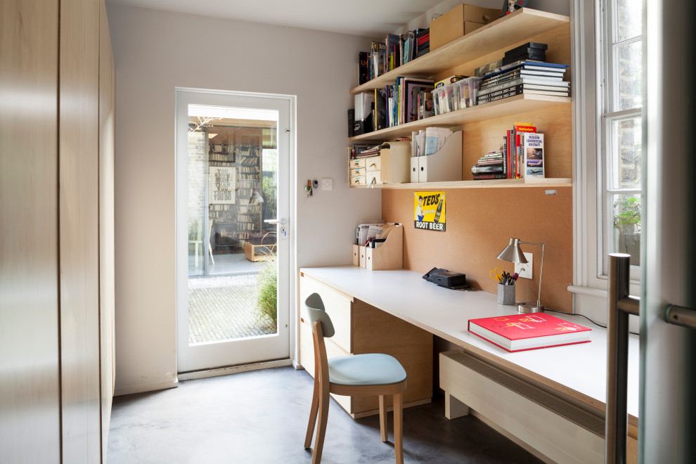 Modern inredning av ett litet hemmastudio, med gula väggar, målat trägolv, en öppen vedspis, en spiselkrans i metall, ett inbyggt skrivbord och grått golv