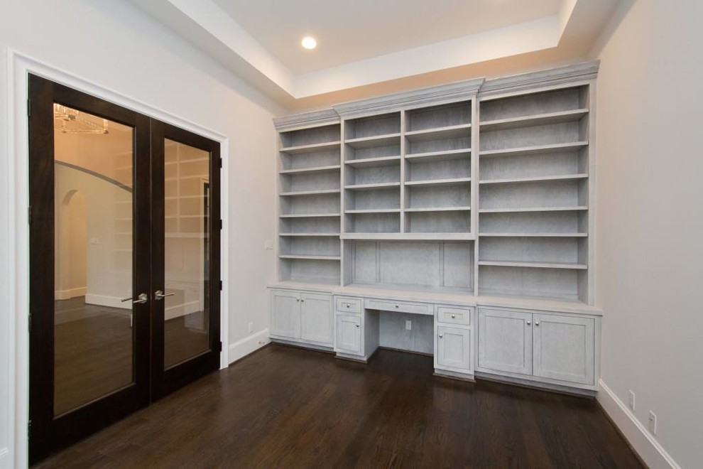 Cette image montre un grand bureau design avec une bibliothèque ou un coin lecture, un mur gris, parquet foncé, un bureau intégré et un sol marron.