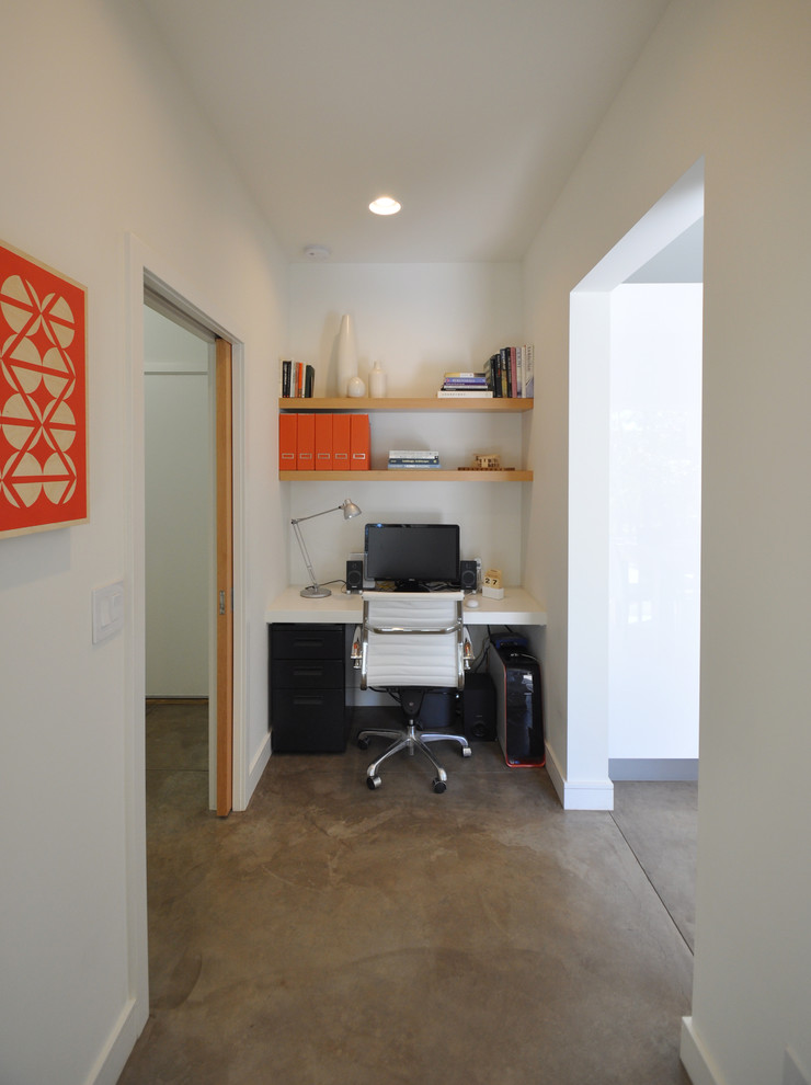 Inredning av ett modernt arbetsrum, med betonggolv, vita väggar och ett inbyggt skrivbord
