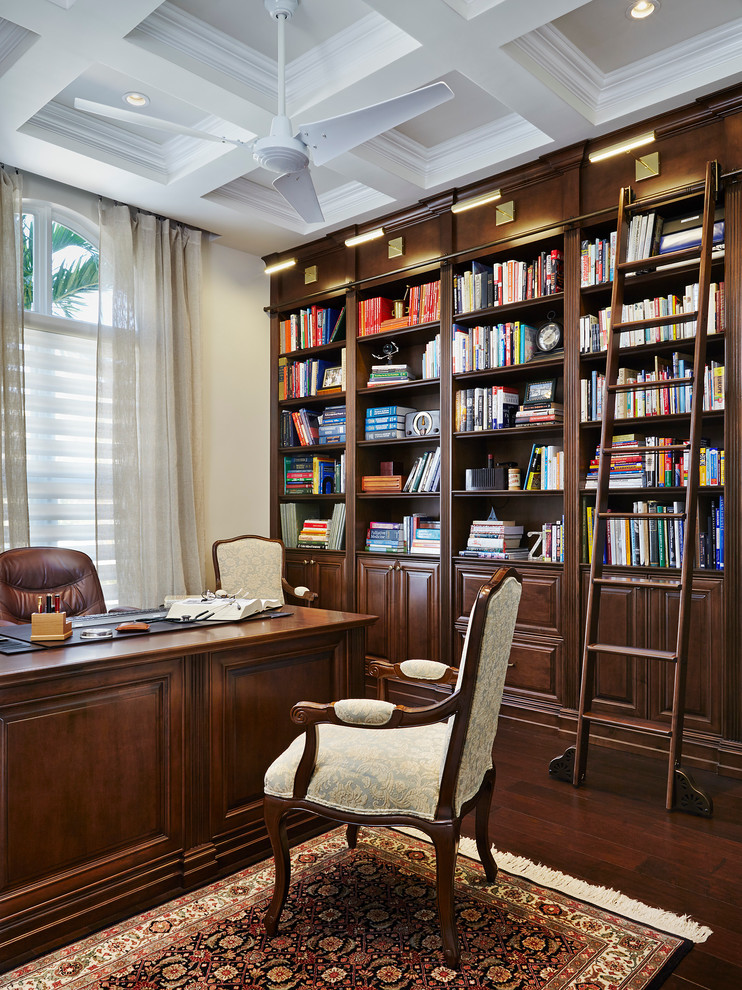 Elegant freestanding desk dark wood floor home office library photo in Miami with beige walls