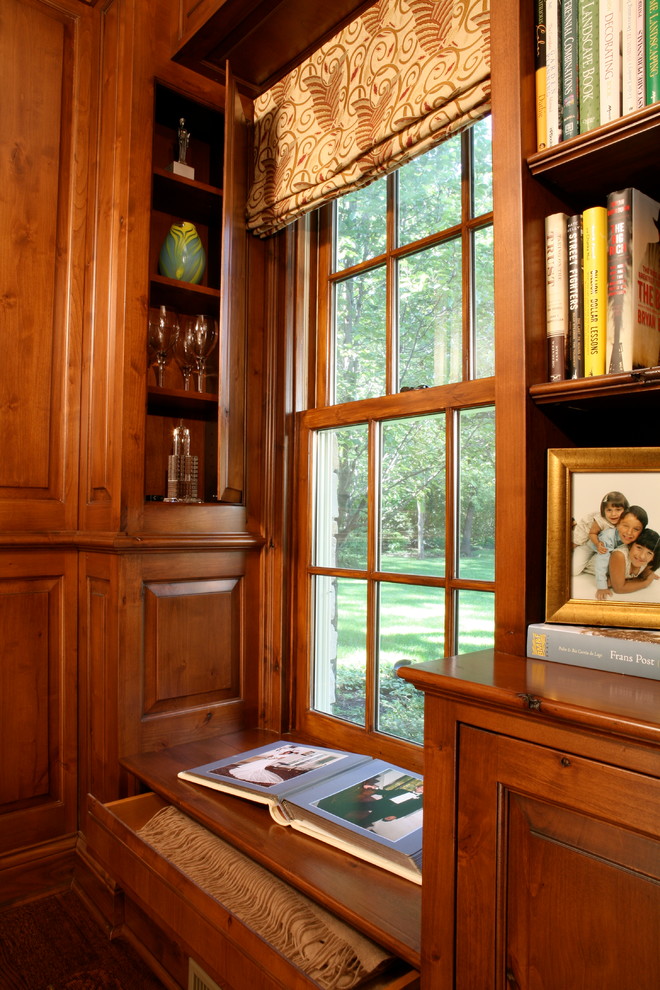 Inredning av ett klassiskt stort hemmabibliotek, med bruna väggar, mörkt trägolv, en standard öppen spis, en spiselkrans i trä och ett fristående skrivbord