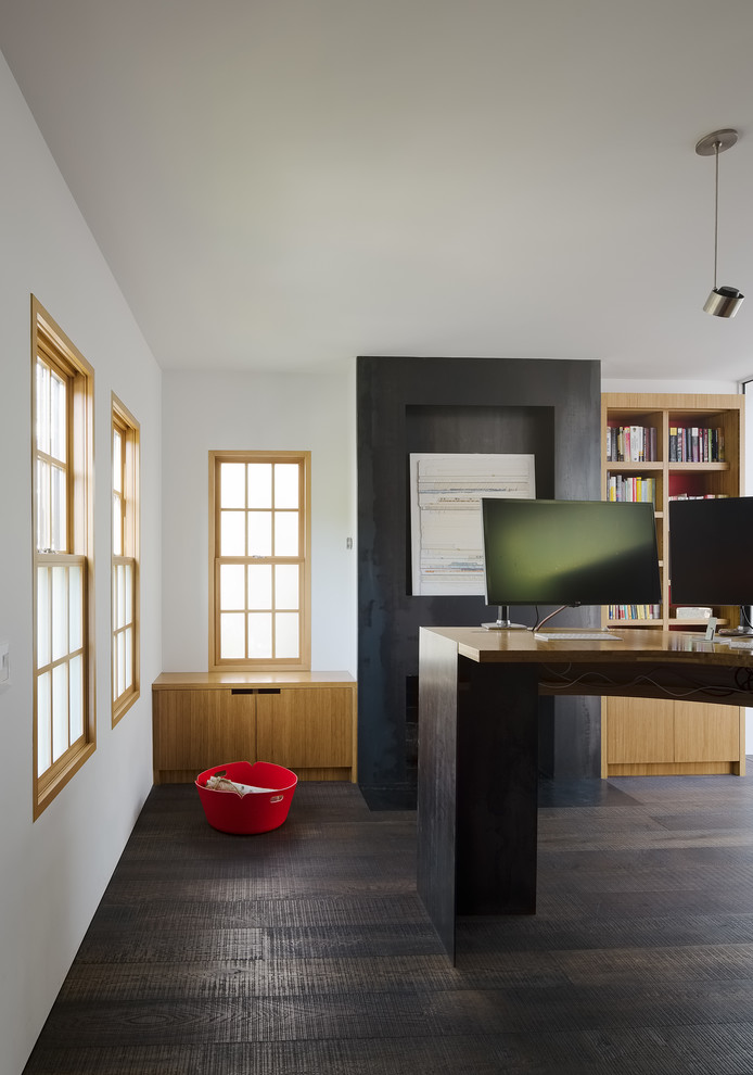 Ejemplo de despacho actual con biblioteca, paredes blancas, suelo de madera oscura, todas las chimeneas, marco de chimenea de metal, escritorio independiente y suelo negro