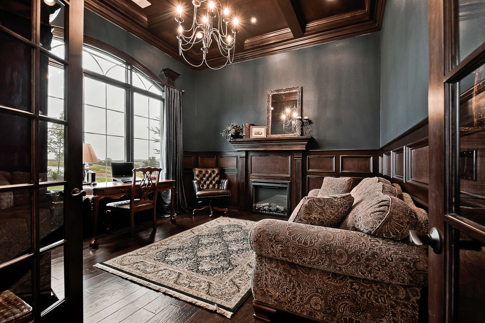 他の地域にある高級な広いトラディショナルスタイルのおしゃれな書斎 (青い壁、濃色無垢フローリング、標準型暖炉、木材の暖炉まわり、自立型机、茶色い床) の写真