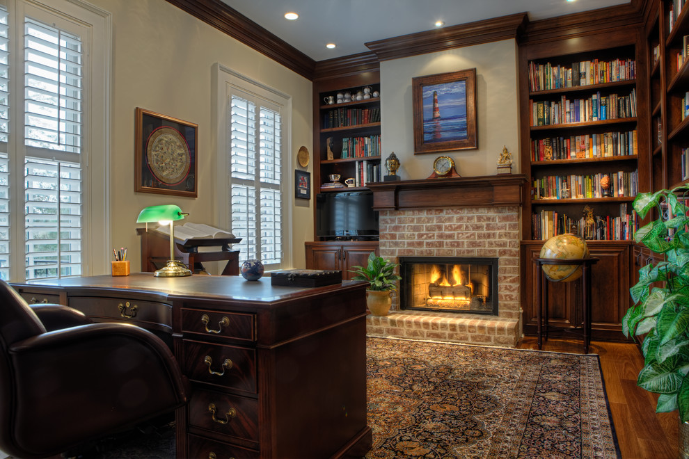 Cette photo montre un bureau chic avec un manteau de cheminée en brique, une cheminée standard, un sol en bois brun, un bureau indépendant et une bibliothèque ou un coin lecture.