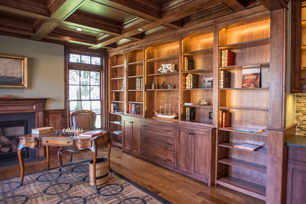 Inspiration för stora klassiska hemmabibliotek, med beige väggar, mellanmörkt trägolv, en standard öppen spis, en spiselkrans i betong, ett fristående skrivbord och brunt golv