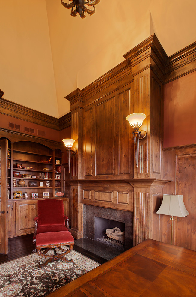 Bild på ett mellanstort vintage hemmabibliotek, med mörkt trägolv, en standard öppen spis, ett fristående skrivbord, en spiselkrans i sten och orange väggar