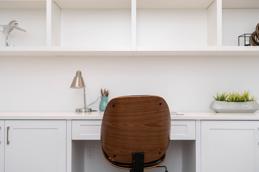 Diseño de despacho clásico renovado de tamaño medio con biblioteca, paredes blancas, suelo de madera en tonos medios y escritorio empotrado
