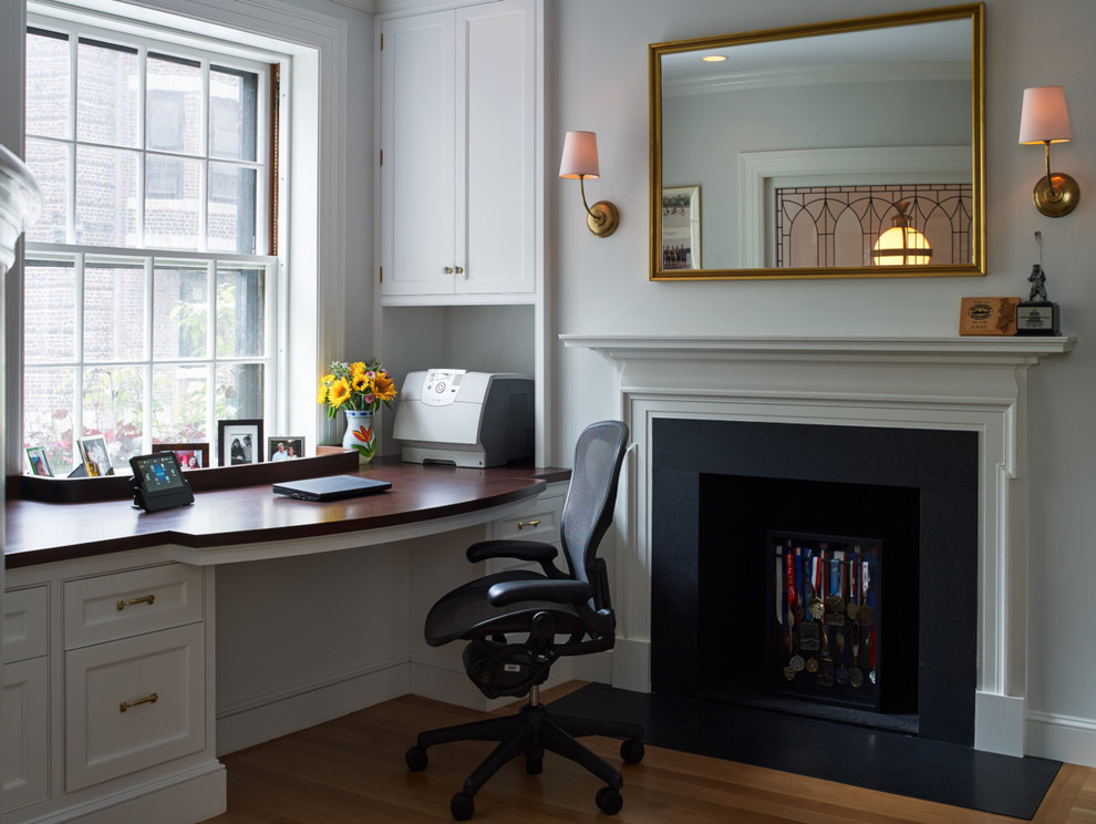 Mid-sized elegant built-in desk light wood floor and brown floor study room photo in Boston with gray walls, a standard fireplace and a stone fireplace