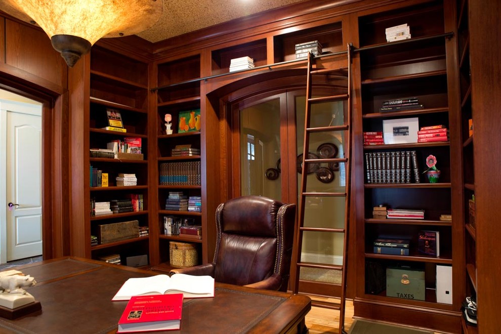 Exempel på ett stort klassiskt hemmabibliotek, med bruna väggar, ljust trägolv och ett fristående skrivbord