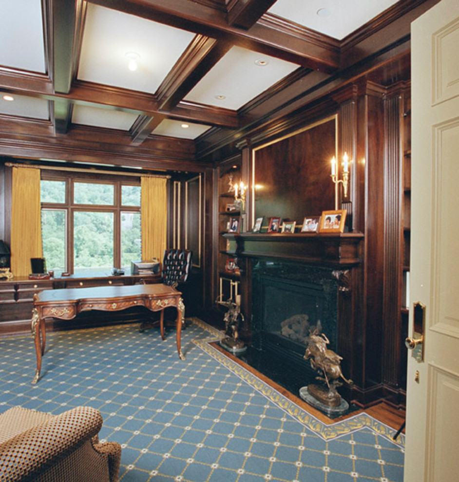 Exempel på ett mellanstort hemmabibliotek, med bruna väggar, heltäckningsmatta, en standard öppen spis, en spiselkrans i trä och ett fristående skrivbord