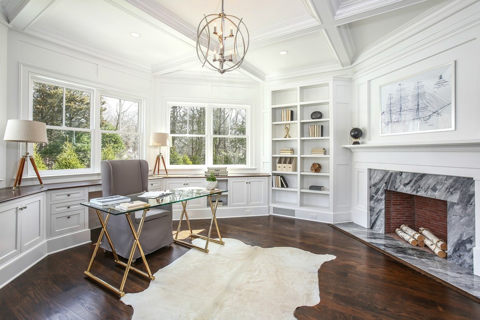 This is an example of a medium sized traditional study in New York with white walls, dark hardwood flooring, a standard fireplace, a stone fireplace surround, a freestanding desk and brown floors.