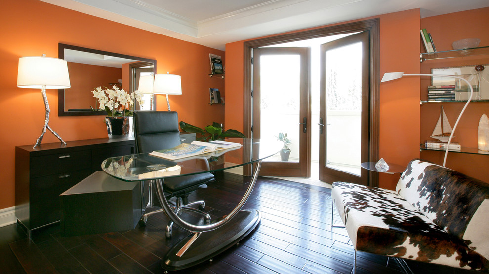 Modern inredning av ett stort arbetsrum, med orange väggar, mörkt trägolv och ett fristående skrivbord