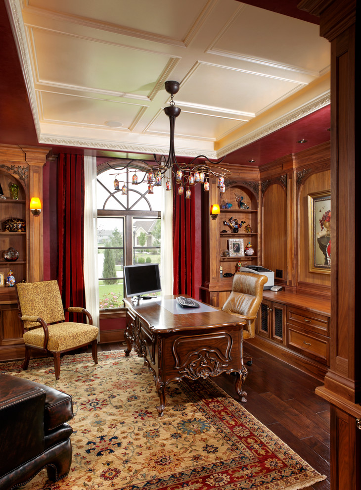 Großes Klassisches Arbeitszimmer ohne Kamin mit roter Wandfarbe, dunklem Holzboden und freistehendem Schreibtisch in Sonstige