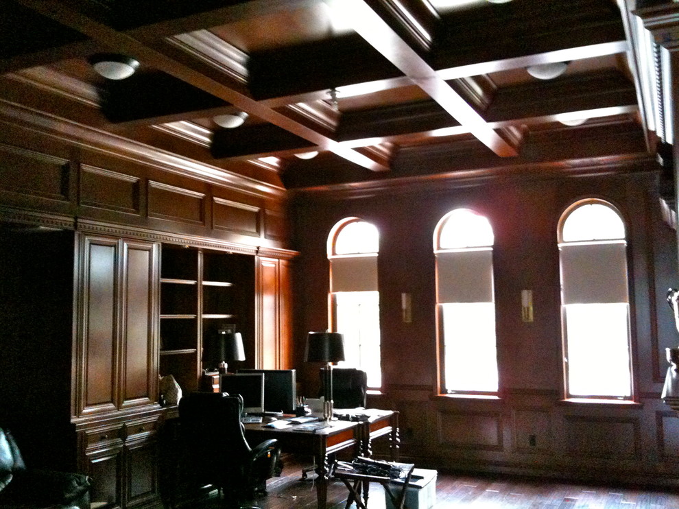 На фото: большой домашняя библиотека в классическом стиле с коричневыми стенами, темным паркетным полом, стандартным камином, фасадом камина из дерева, встроенным рабочим столом и коричневым полом
