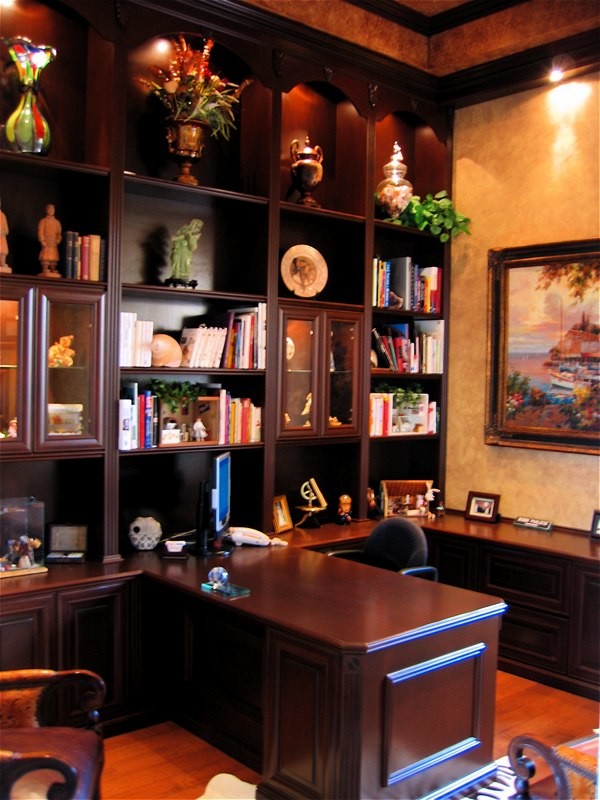 Modelo de despacho clásico grande con biblioteca, paredes beige, suelo de madera clara, escritorio empotrado y suelo marrón