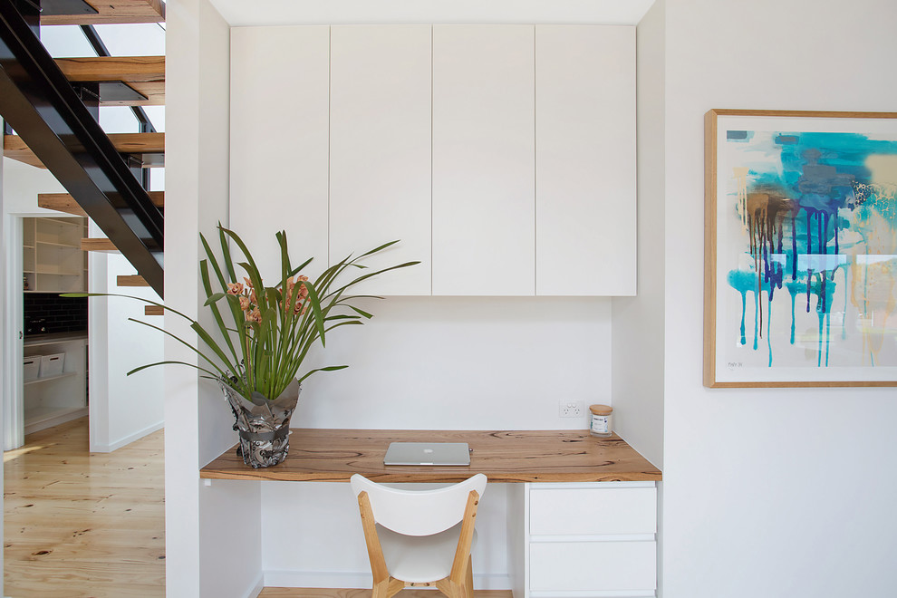 Modernes Arbeitszimmer mit weißer Wandfarbe, hellem Holzboden, Einbau-Schreibtisch und beigem Boden in Sonstige