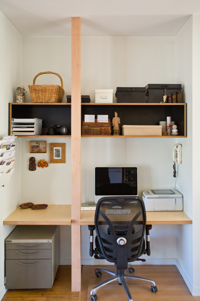 Photo of a small contemporary study in Melbourne with light hardwood flooring, a built-in desk and white walls.