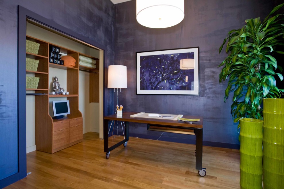 Diseño de despacho asiático sin chimenea con paredes púrpuras, suelo de madera clara y escritorio independiente