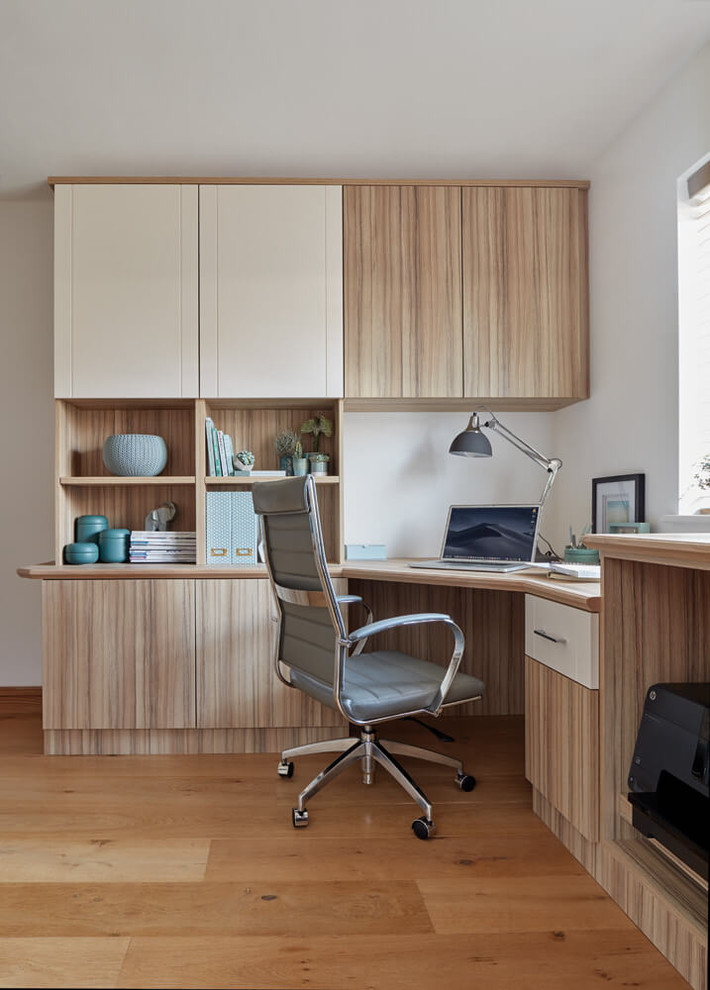 This is an example of a medium sized contemporary home office in Manchester with beige walls, medium hardwood flooring, a built-in desk and brown floors.