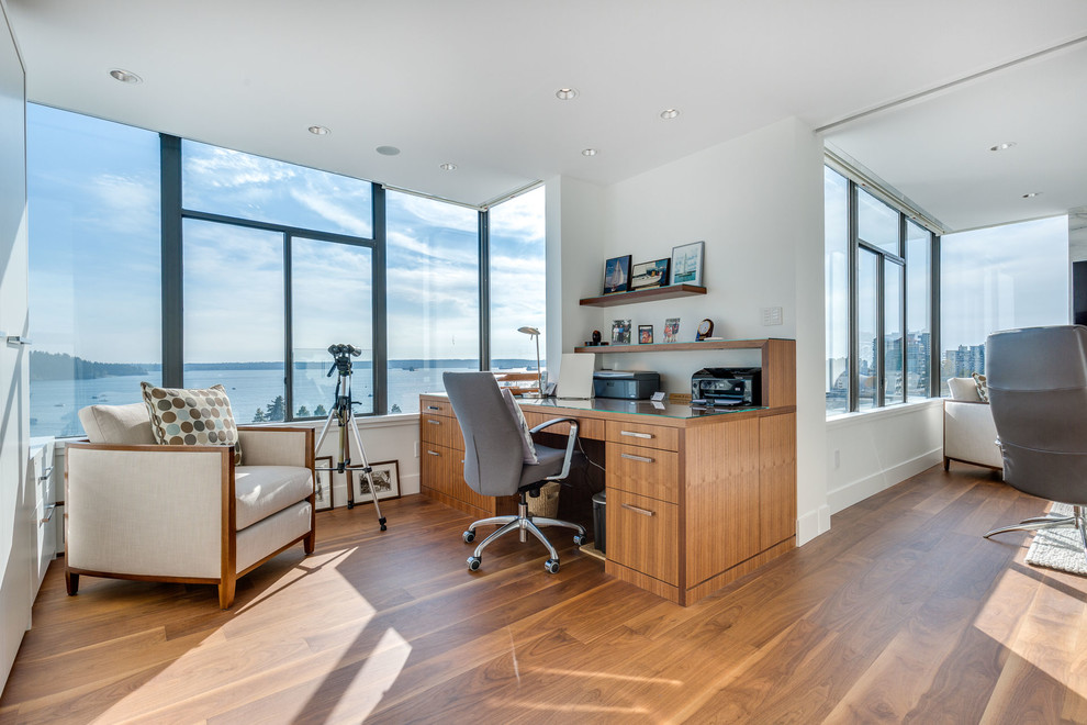Study room - contemporary built-in desk medium tone wood floor study room idea in Vancouver with white walls