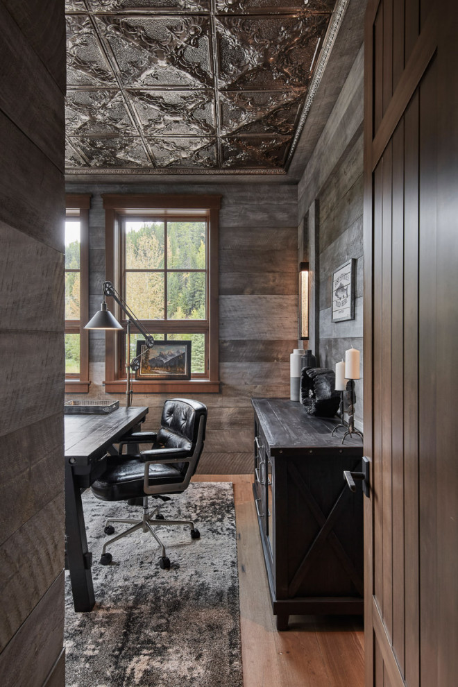 Rustik inredning av ett mellanstort arbetsrum, med grå väggar, mellanmörkt trägolv, ett fristående skrivbord och brunt golv