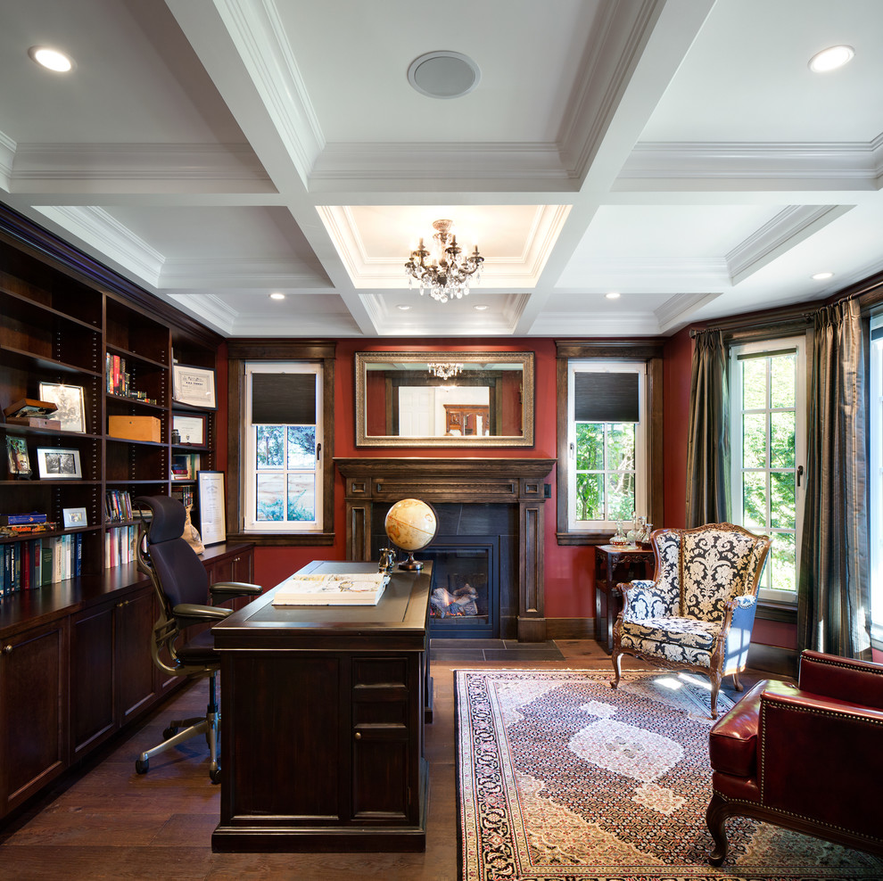 Ejemplo de despacho clásico de tamaño medio con paredes rojas, suelo de madera oscura, todas las chimeneas y escritorio independiente