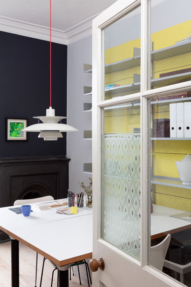 Diseño de estudio contemporáneo de tamaño medio con paredes amarillas, suelo de madera clara, chimenea de esquina, marco de chimenea de metal y escritorio independiente