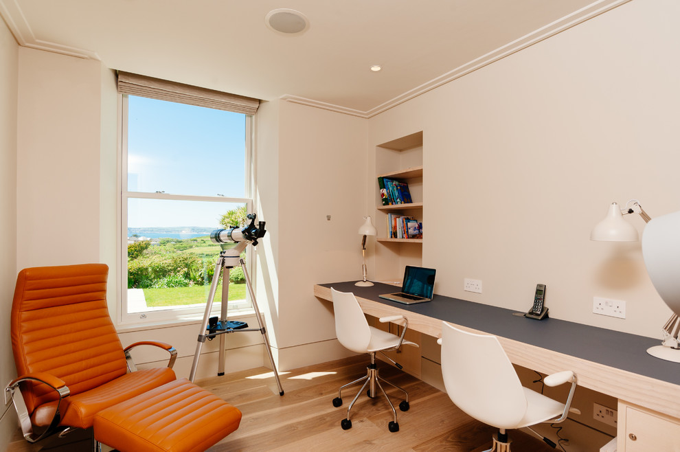 Ejemplo de despacho costero de tamaño medio con paredes blancas, suelo de madera clara y escritorio empotrado