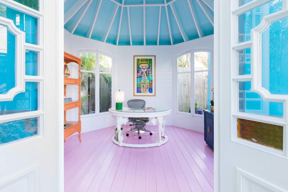 Diseño de despacho tropical con paredes blancas, suelo de madera pintada, escritorio independiente y suelo rosa