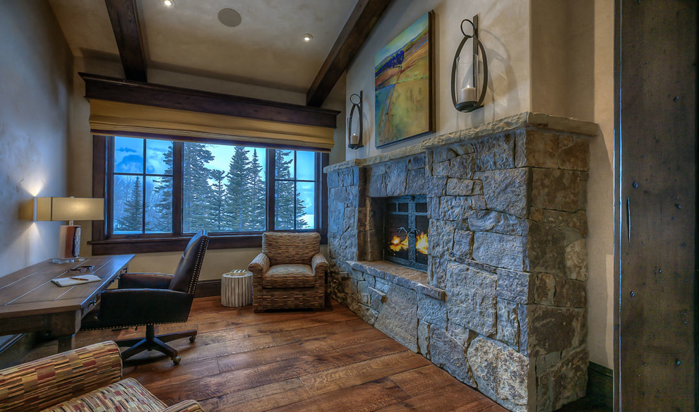 This is an example of a large rustic study in Salt Lake City with beige walls, medium hardwood flooring, a two-sided fireplace, a stone fireplace surround and a freestanding desk.