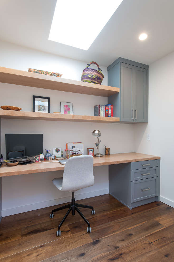 Cette photo montre un bureau tendance de taille moyenne avec un mur blanc, parquet foncé, aucune cheminée, un bureau intégré et un sol marron.