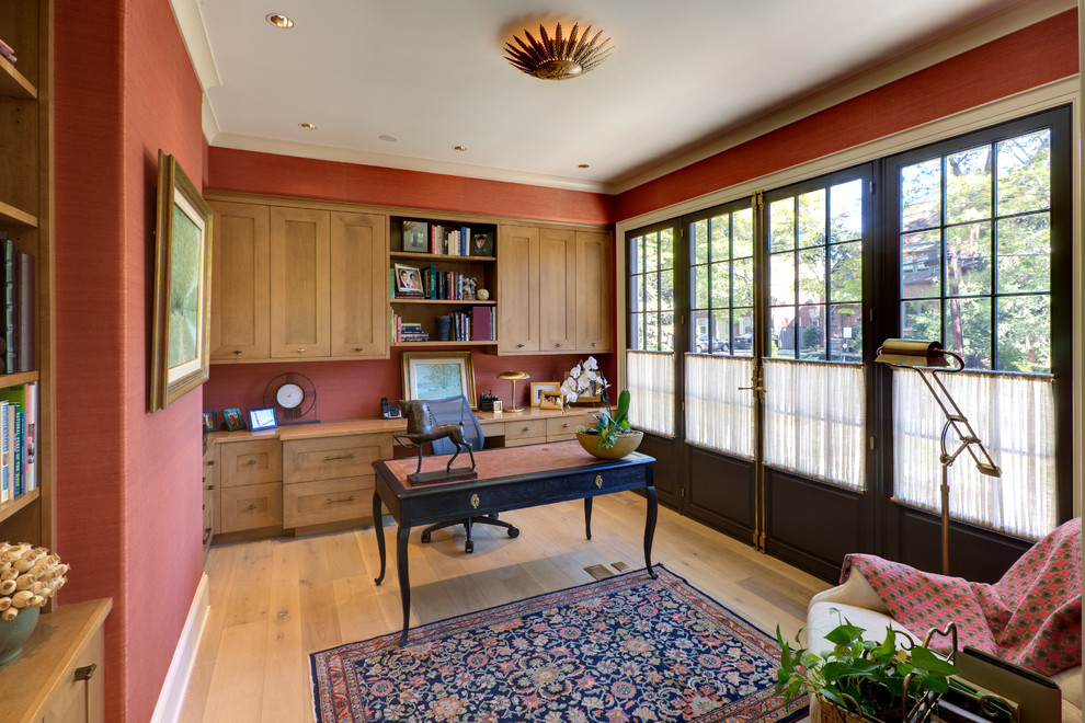 Diseño de despacho tradicional sin chimenea con paredes rojas, suelo de madera clara y escritorio independiente