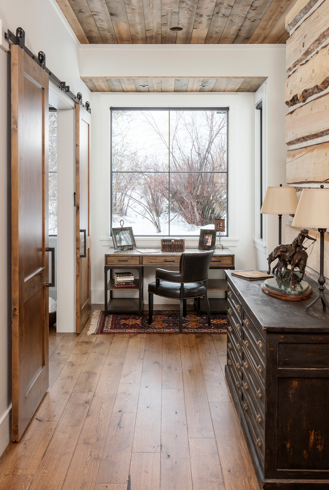 Country Arbeitszimmer mit weißer Wandfarbe, braunem Holzboden, freistehendem Schreibtisch und braunem Boden in Salt Lake City