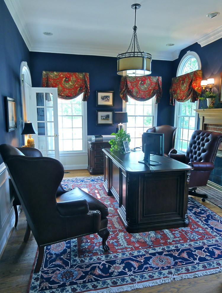 Inredning av ett klassiskt mellanstort hemmabibliotek, med blå väggar, mellanmörkt trägolv och ett fristående skrivbord