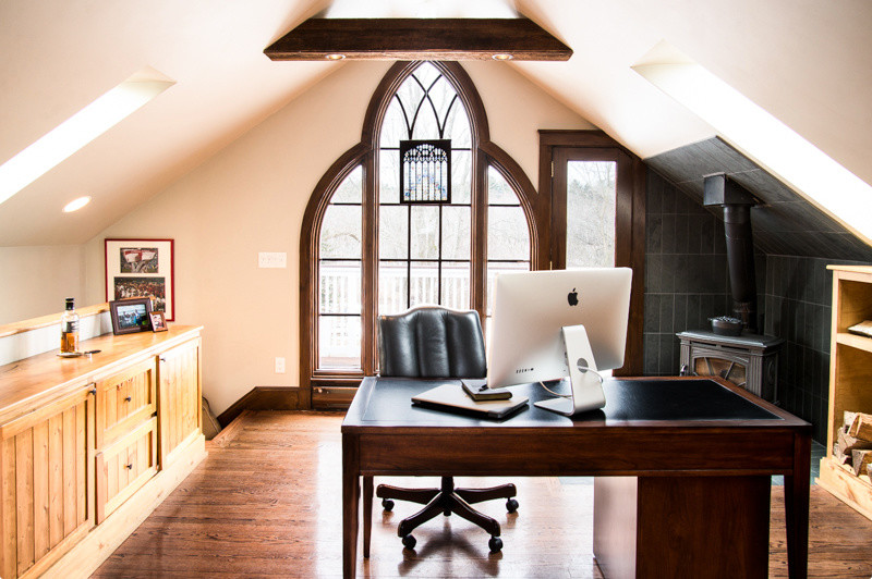 Uriges Arbeitszimmer mit Arbeitsplatz, weißer Wandfarbe, braunem Holzboden, Kaminofen, Kaminumrandung aus Stein, freistehendem Schreibtisch und braunem Boden in Boston