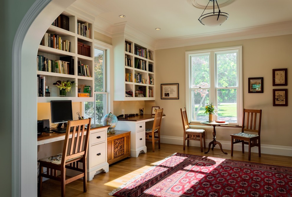 Inredning av ett klassiskt hemmabibliotek, med beige väggar, ljust trägolv och ett inbyggt skrivbord