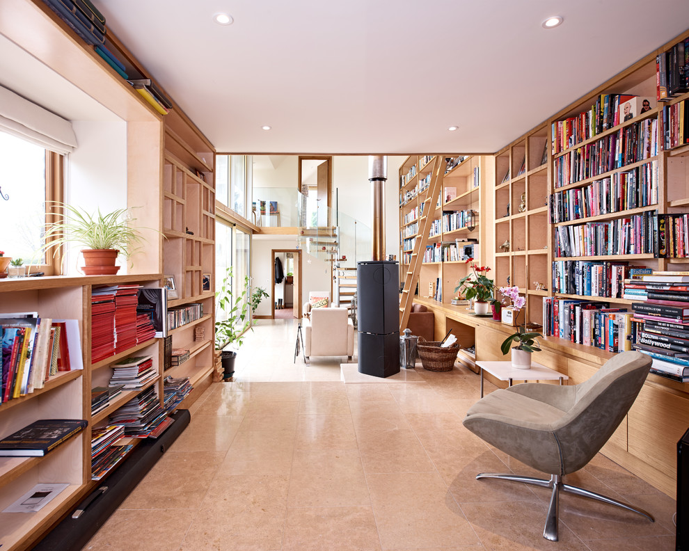 Cette photo montre un bureau tendance de taille moyenne avec une bibliothèque ou un coin lecture, un mur blanc, un sol en calcaire, un poêle à bois, un bureau intégré et un sol beige.