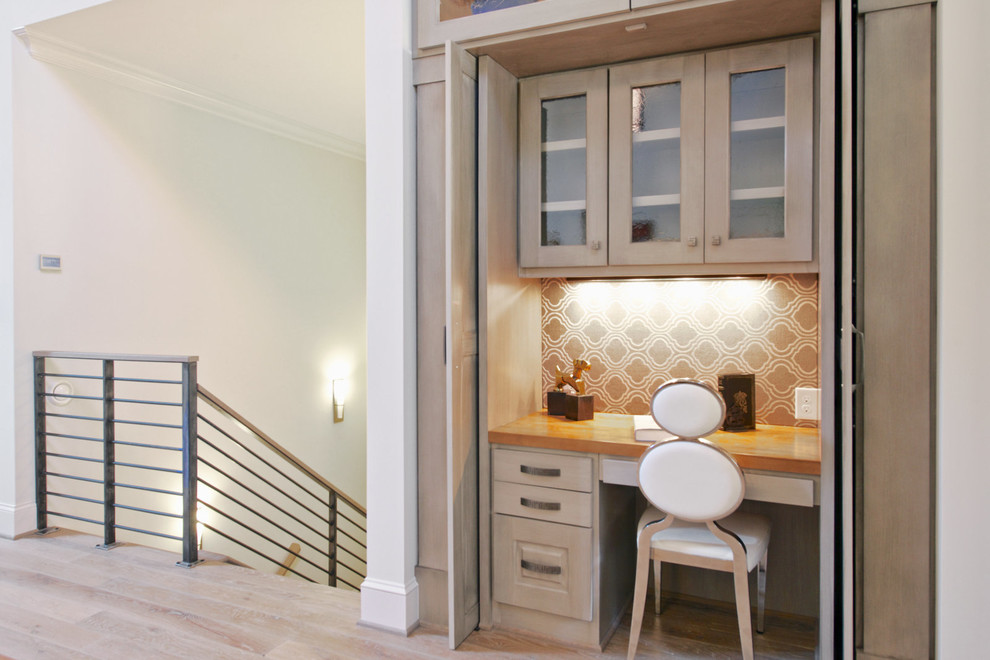 Modelo de despacho actual pequeño sin chimenea con escritorio empotrado, paredes beige, suelo de madera clara y suelo beige