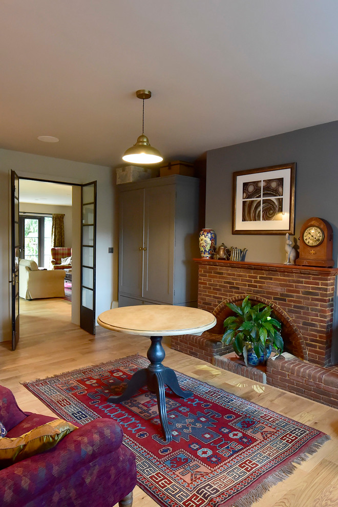 Study room - mid-sized mid-century modern medium tone wood floor and beige floor study room idea in Hertfordshire with gray walls, a standard fireplace and a brick fireplace
