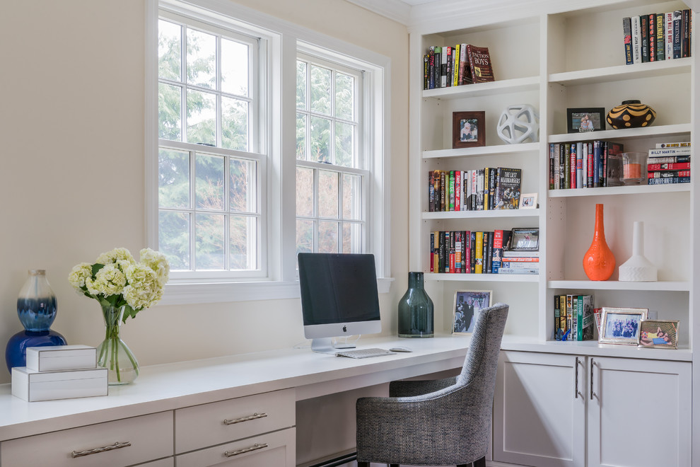 Klassisches Arbeitszimmer mit Arbeitsplatz, Einbau-Schreibtisch, beiger Wandfarbe, dunklem Holzboden, Kamin, Kaminumrandung aus Stein und braunem Boden in Boston