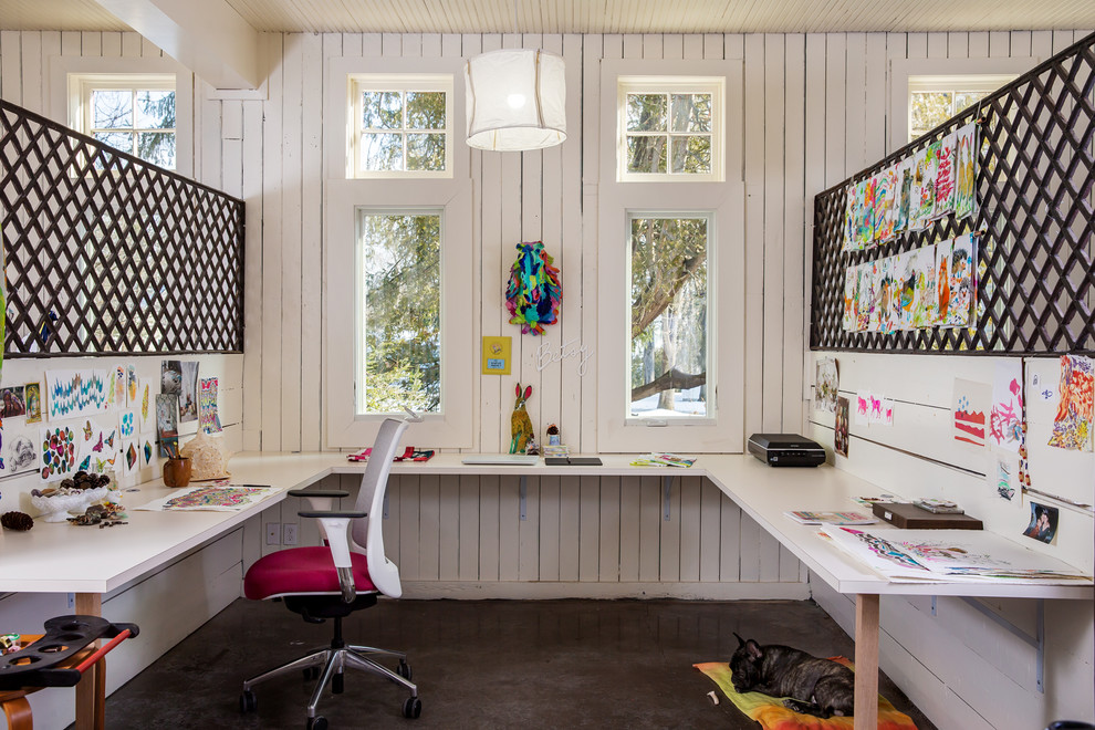 Bild på ett stort funkis hobbyrum, med vita väggar, betonggolv, ett inbyggt skrivbord och grått golv