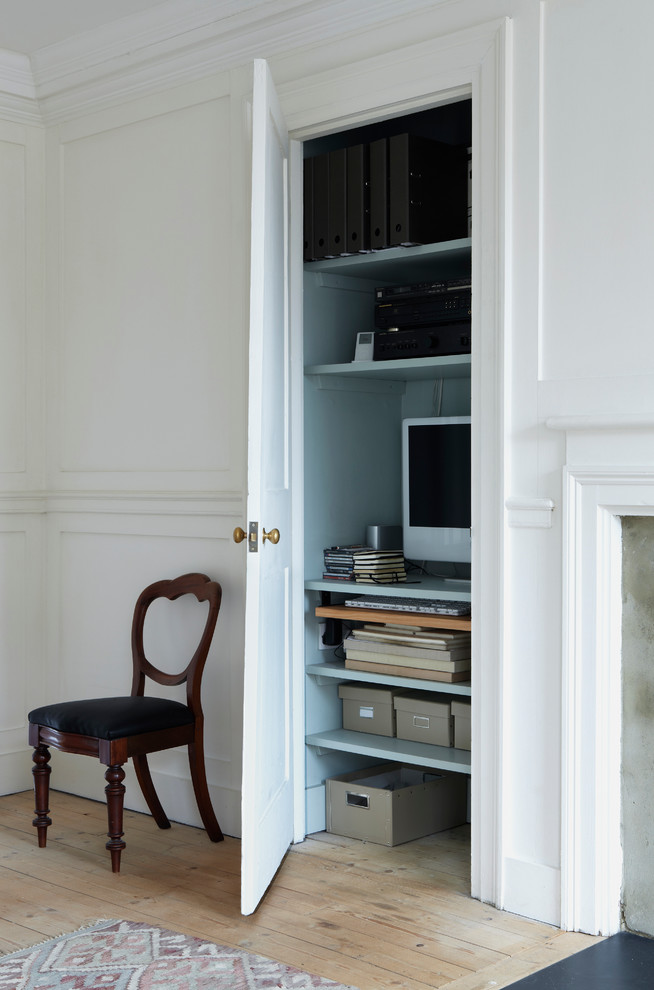 Inredning av ett eklektiskt litet hemmabibliotek, med blå väggar, ljust trägolv och ett inbyggt skrivbord