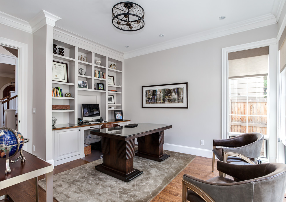 Modelo de despacho clásico renovado con paredes grises, suelo de madera en tonos medios y escritorio independiente