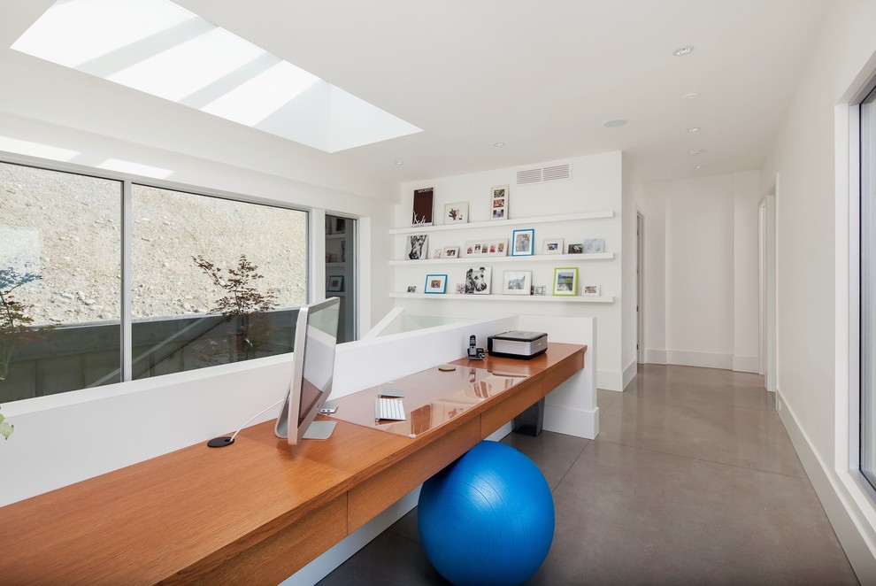 Imagen de despacho actual de tamaño medio con suelo de cemento, paredes blancas y escritorio empotrado
