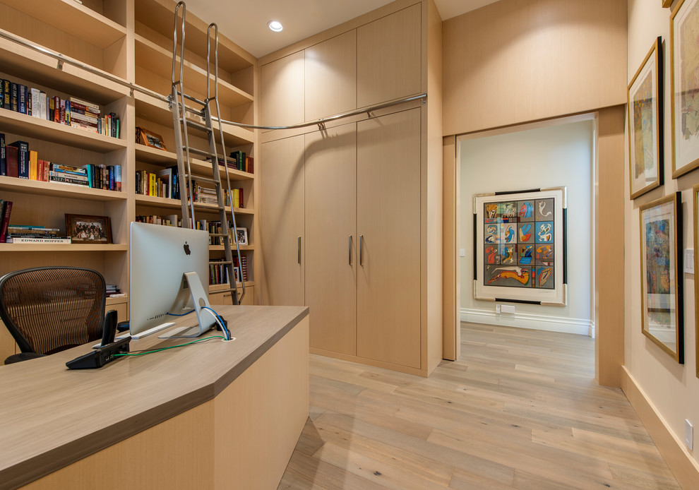 Imagen de despacho actual grande sin chimenea con biblioteca, paredes beige, suelo de madera clara, escritorio independiente y suelo beige