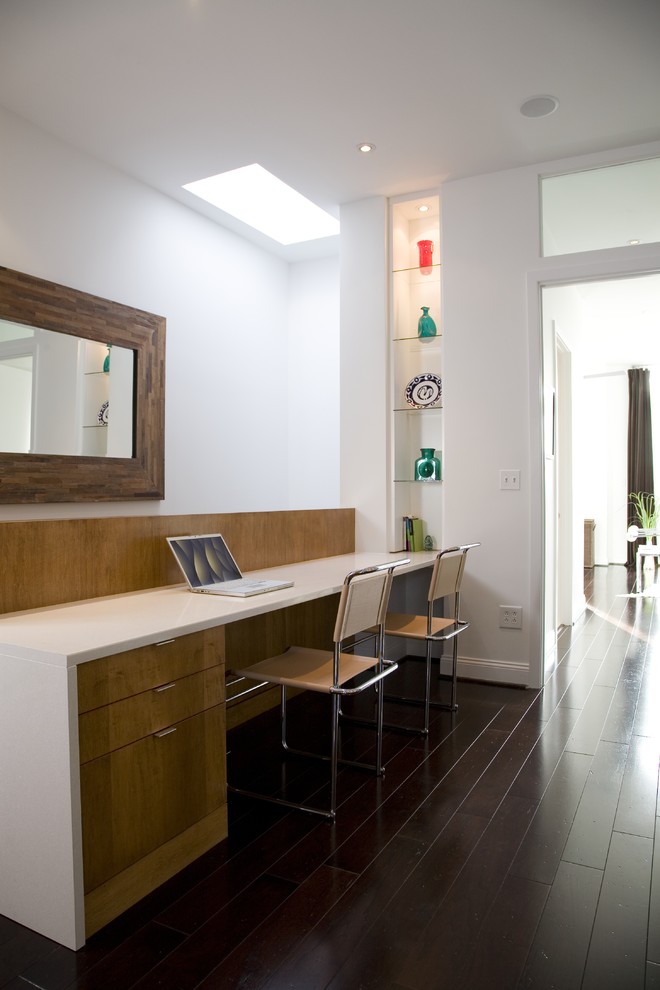 Ejemplo de despacho actual con paredes blancas, suelo de madera oscura y escritorio empotrado