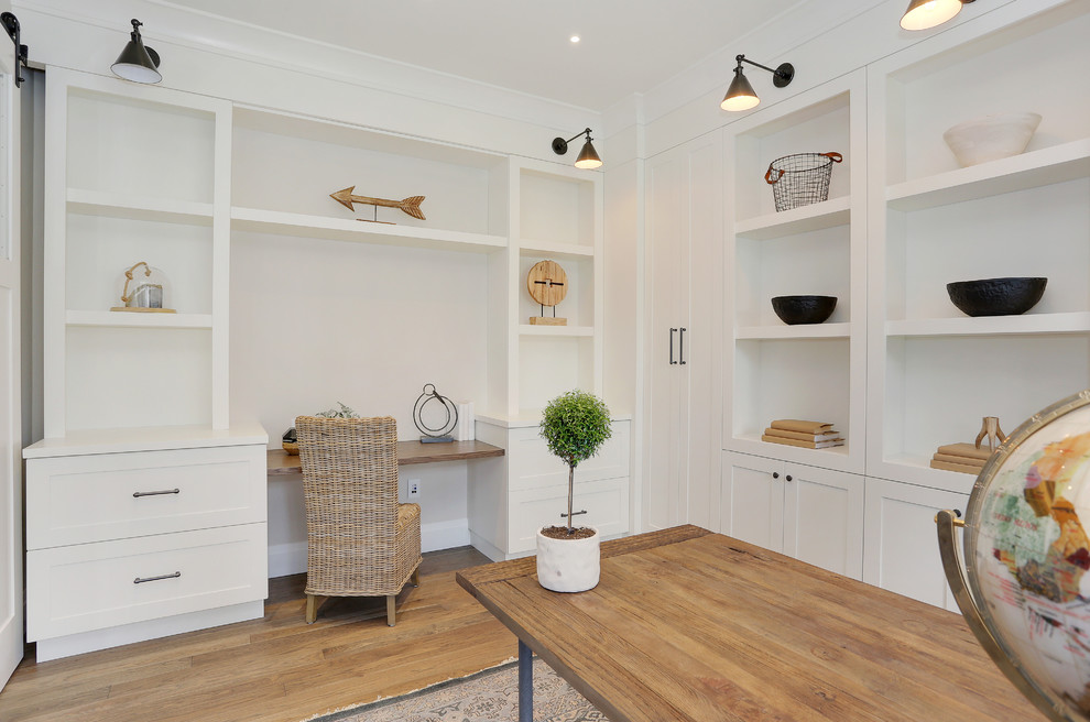 Diseño de despacho de estilo americano grande sin chimenea con paredes blancas, suelo de madera en tonos medios, escritorio independiente y suelo marrón