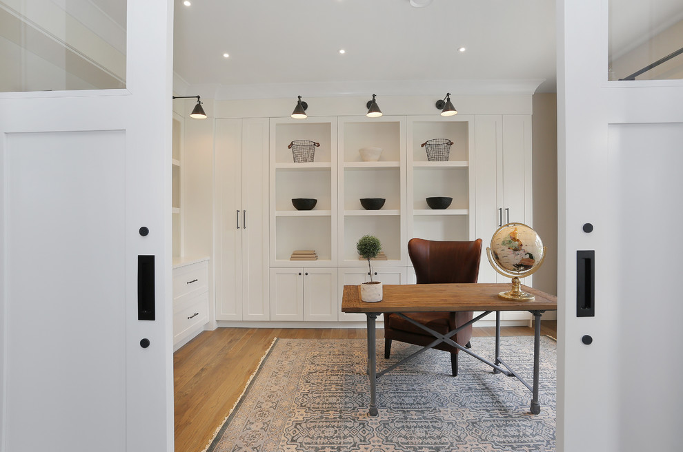 バンクーバーにある広いトラディショナルスタイルのおしゃれなホームオフィス・書斎 (白い壁、無垢フローリング、暖炉なし、自立型机、茶色い床) の写真